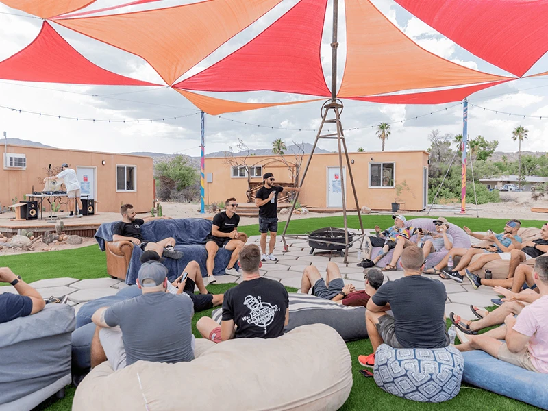 People sitting on the ground with a man standing and talking- The Main Area People sitting on the ground with a man standing and talking- The Main Area